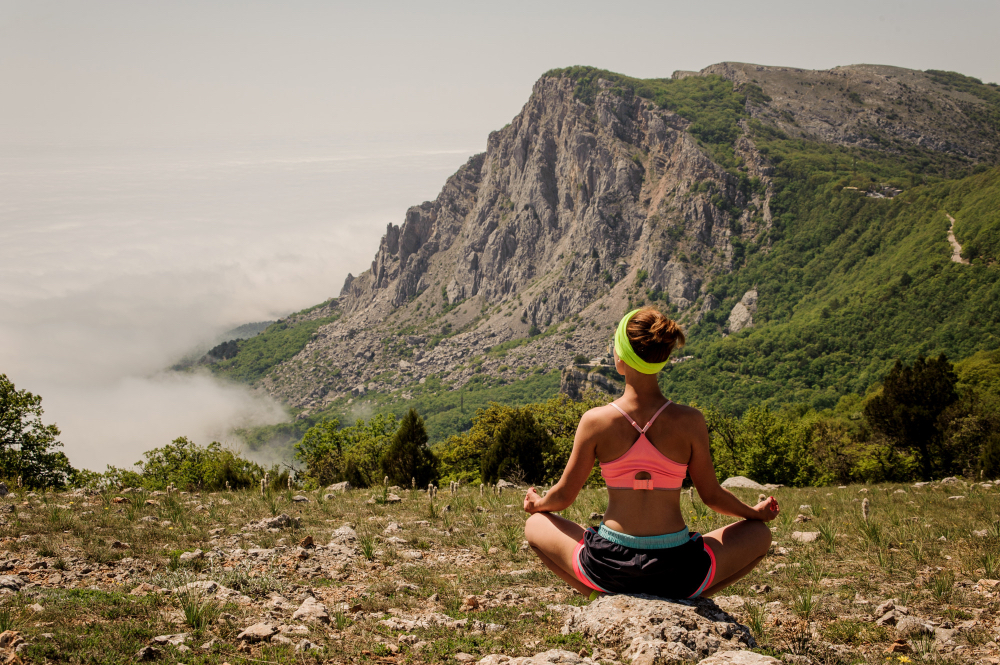Woman practising yoga on a mountain overlooking a misty valley