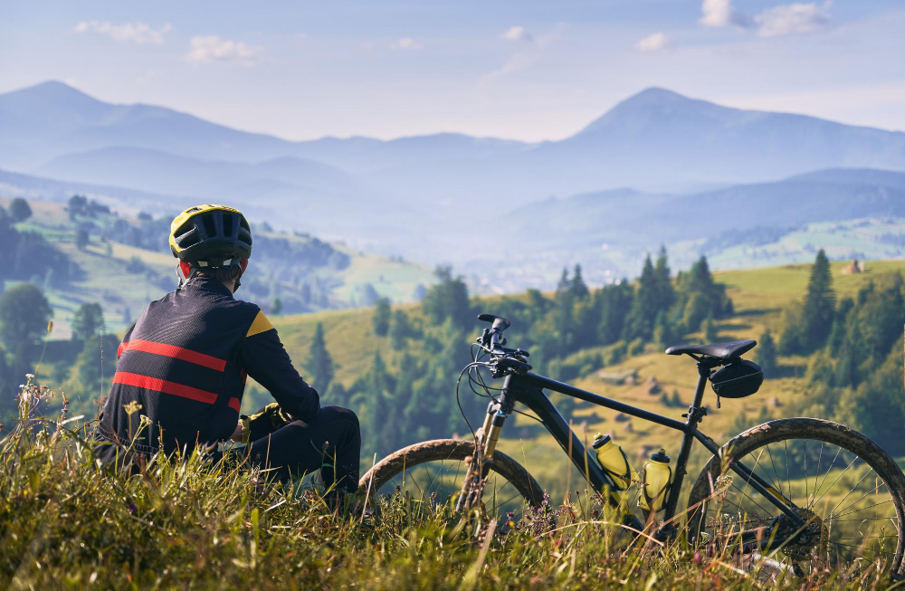 Cyclist resting beside a bike overlooking mountain valleys