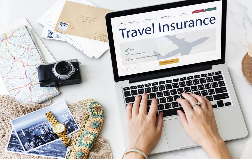 Travel insurance planning with laptop, camera, and travel keepsakes