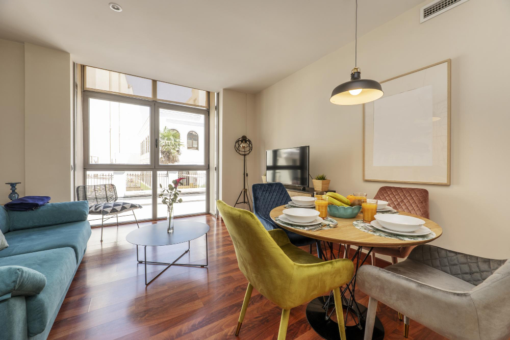 Zonă de dining cu scaune colorate și canapea turcoaz într-un apartament pe termen lung