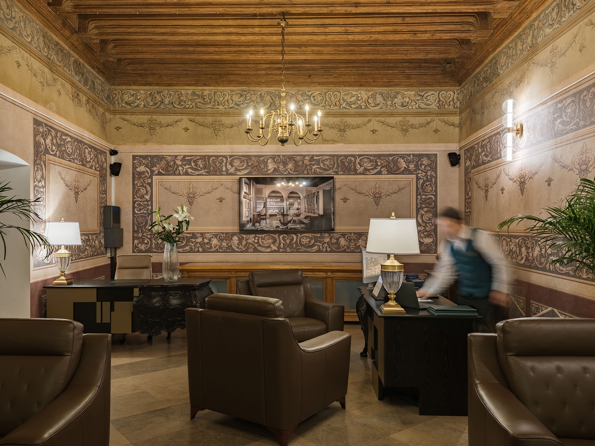 Ornate hotel lobby lounge with frescoed walls, chandelier, and reception desk