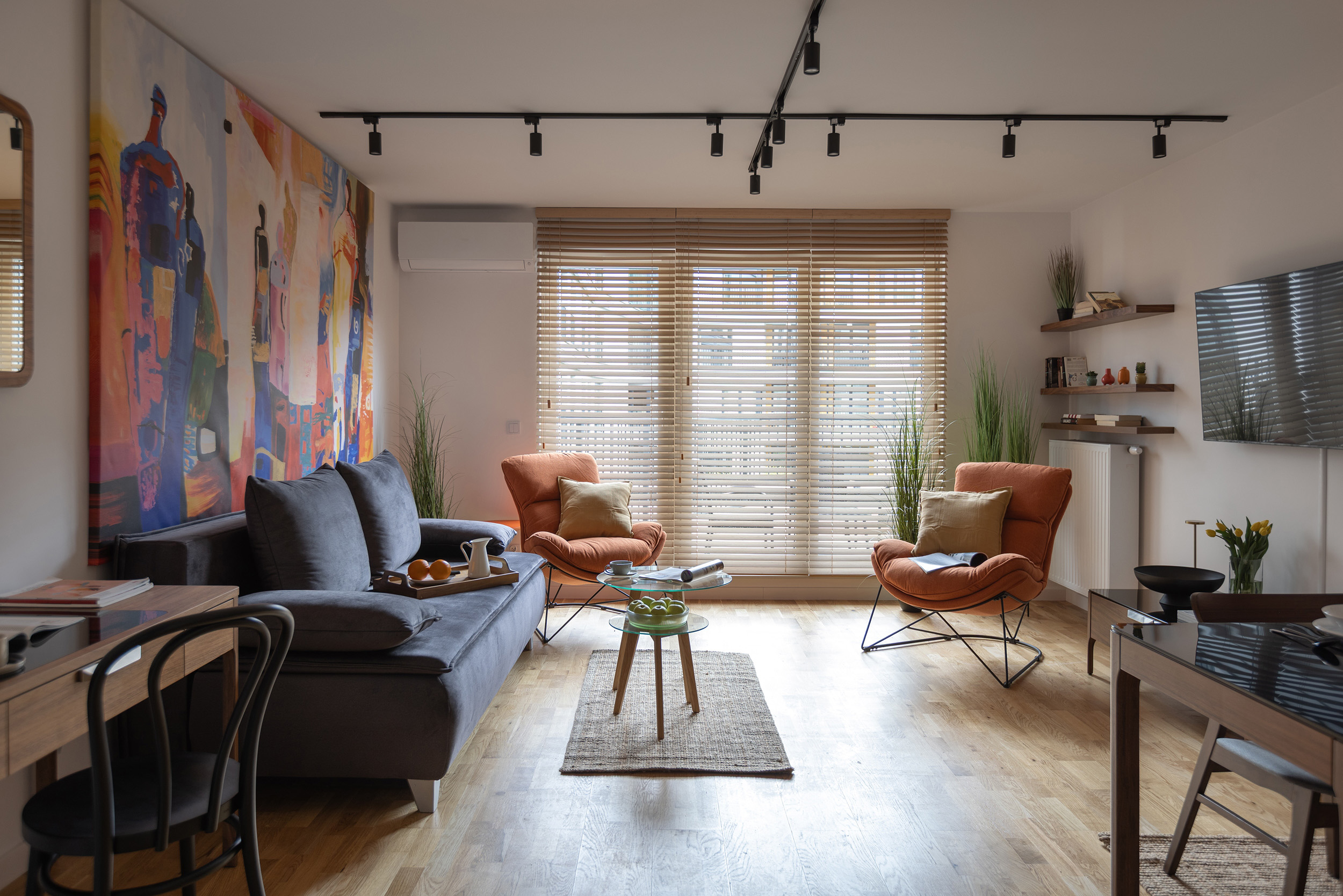 Bright living room with colorful abstract art, gray sofa, and orange accent chairs